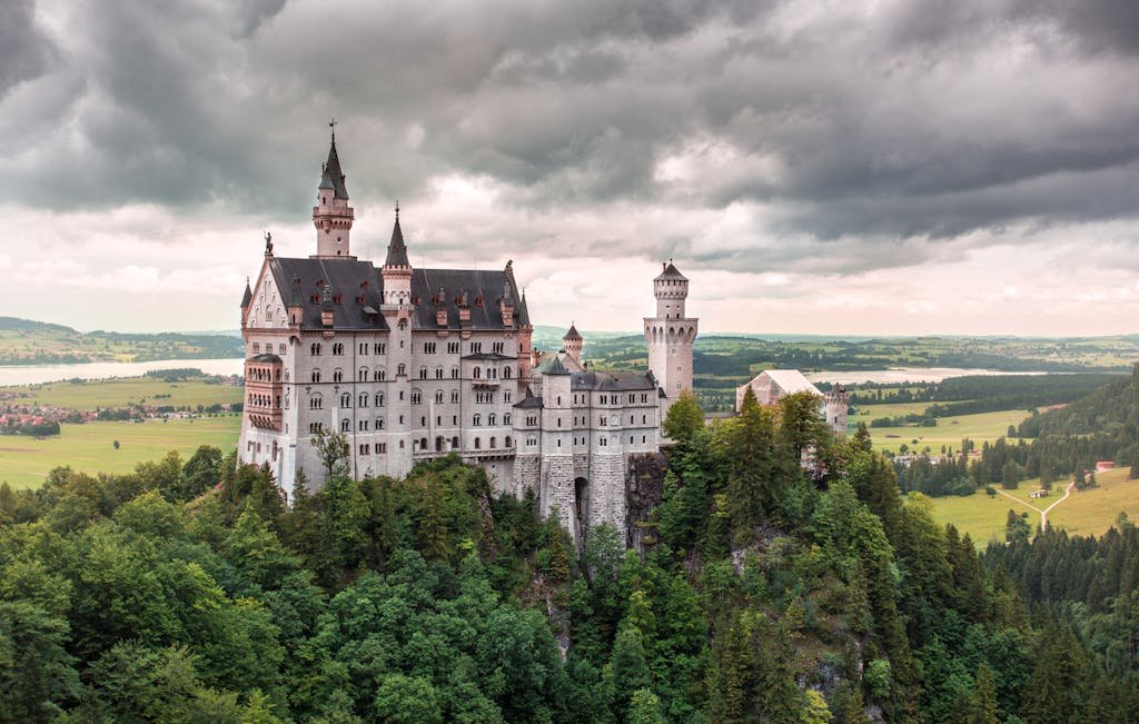 Train tours Switzerland with a stunning view of Neuschwanstein Castle surrounded by lush greenery in Bavaria, Germany.