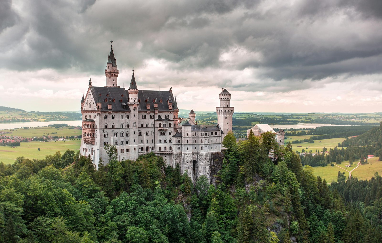 Train tours Switzerland with a stunning view of Neuschwanstein Castle surrounded by lush greenery in Bavaria, Germany.